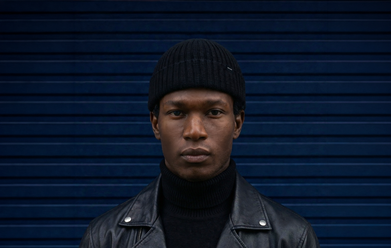 Person wearing a black beanie and leather jacket against a dark blue background